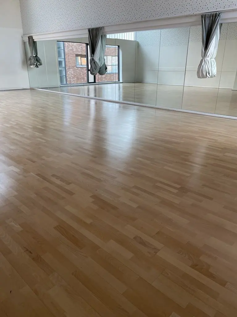 A gymnastics wooden floor perfectly sanded and stained with a view of windows.