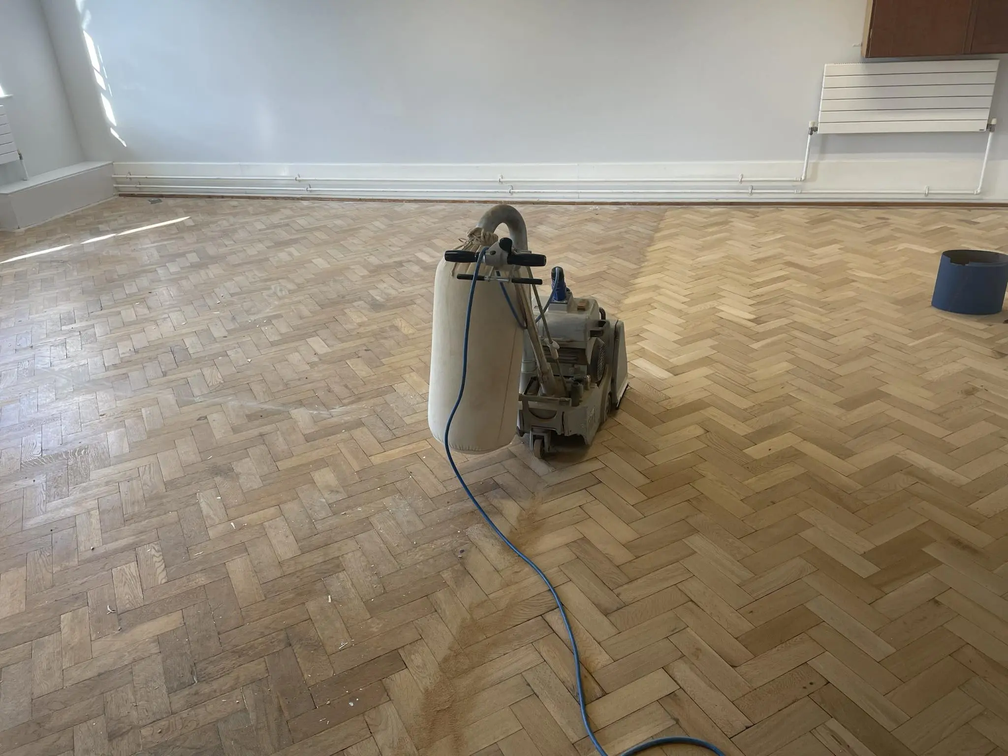 A wooden floor in the process of sanding, with half of it sanded.