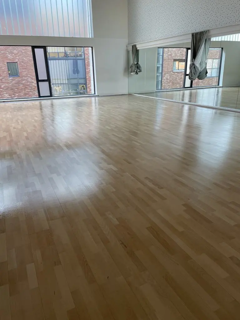 A gymnastics wooden floor perfectly sanded and stained with a view of inside mirrors.