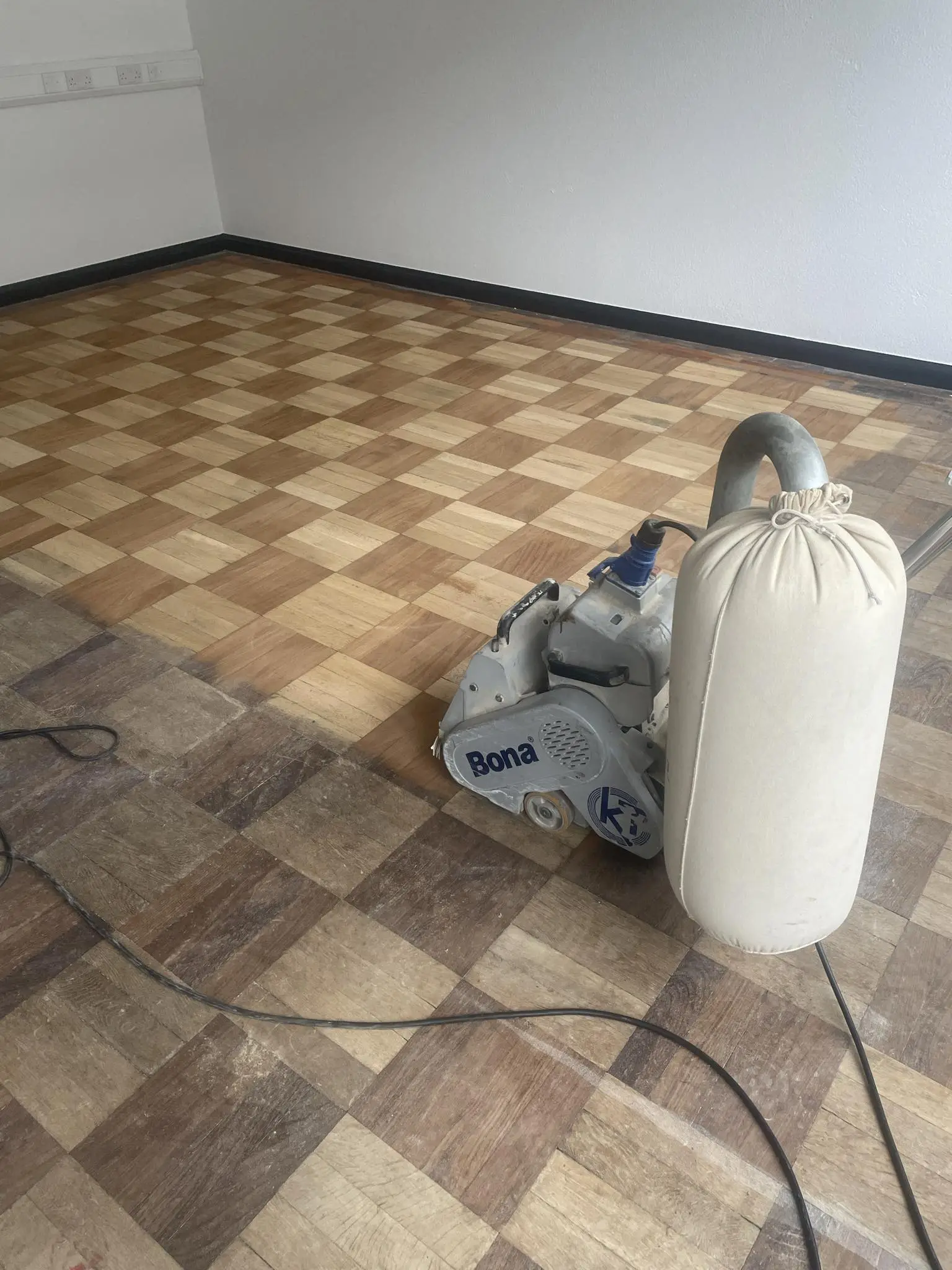 Another wooden floor in the process of sanding, with half of it sanded.