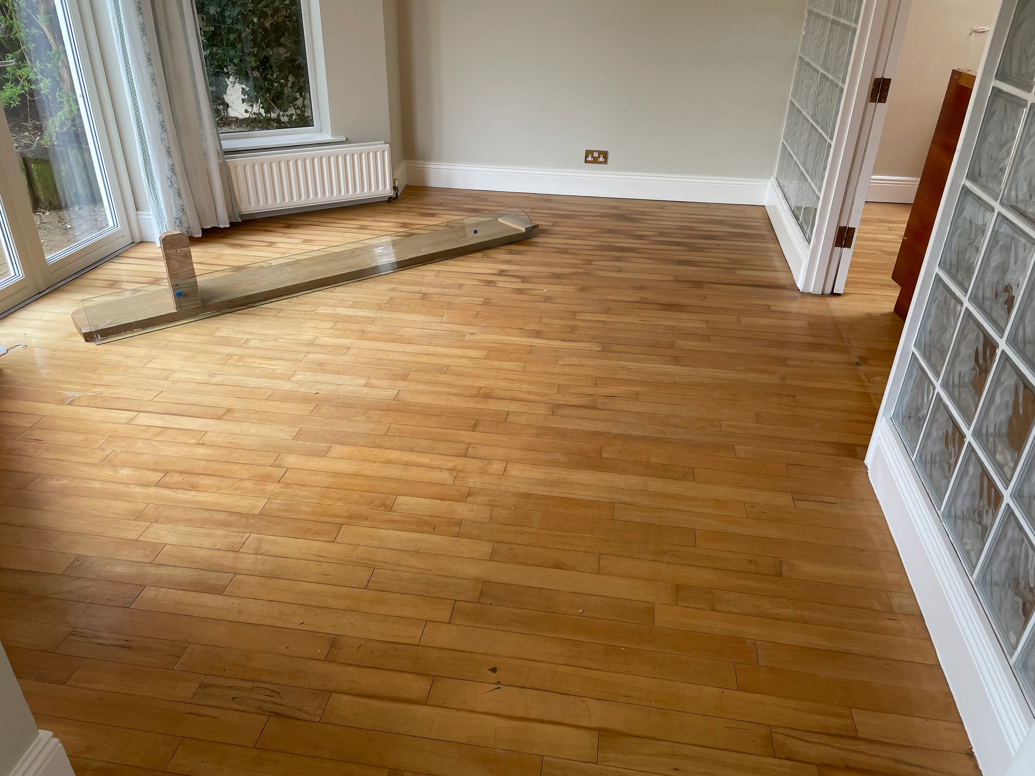 A picture of a wooden floor perfectly sanded and with a nice coat of staining with a bench in background.